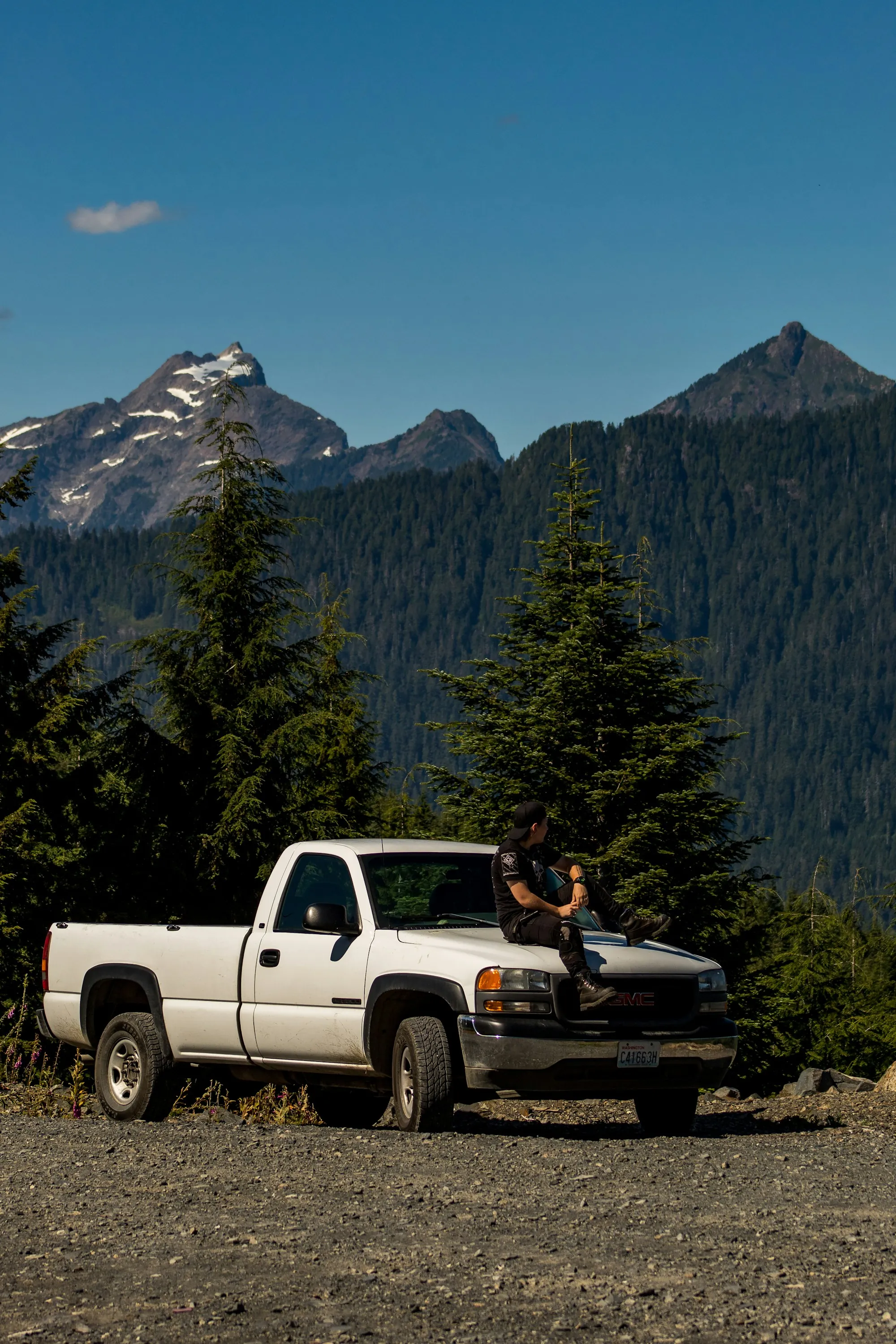 White pickup truck parked below a pine-covered mountain peak