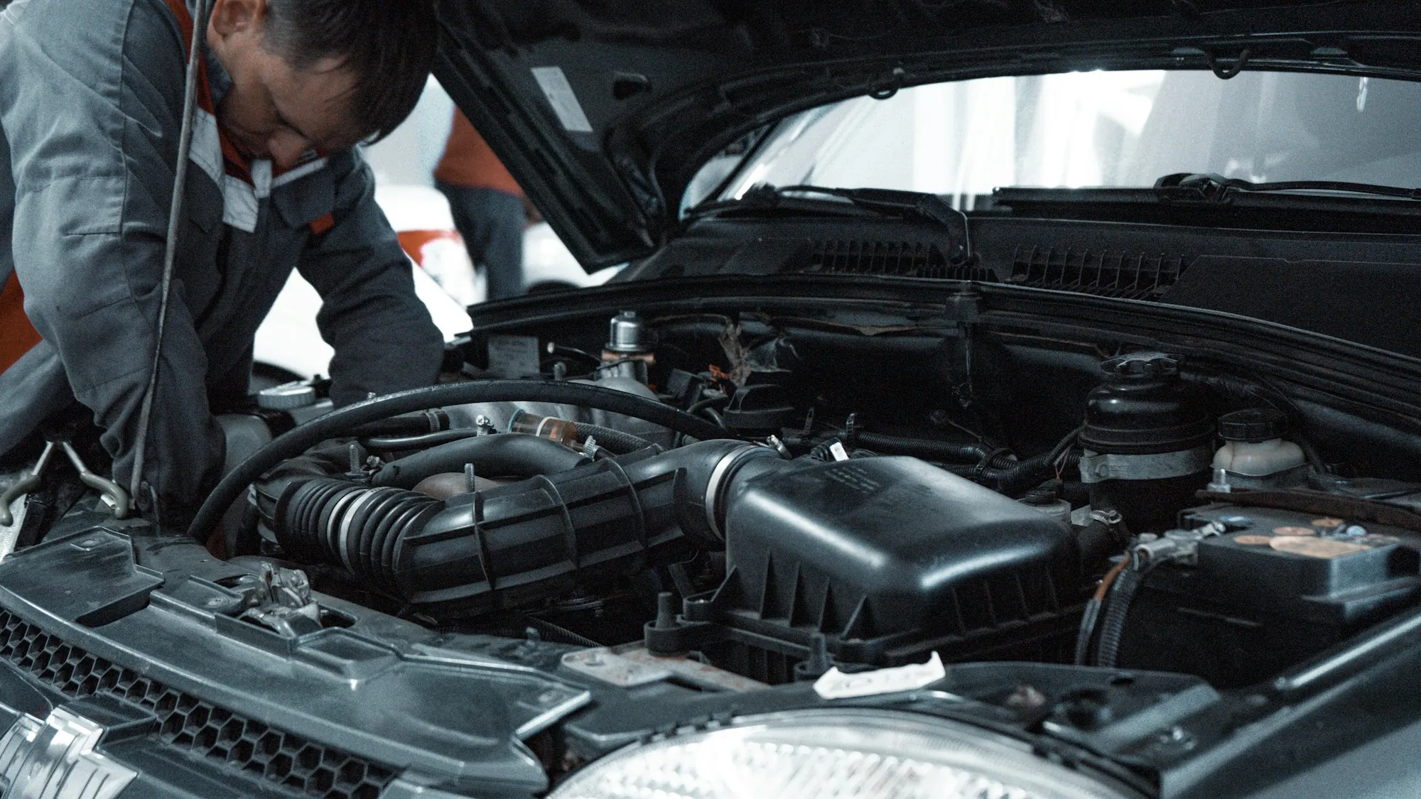 Technician working inside an open engine bay in a repair shop